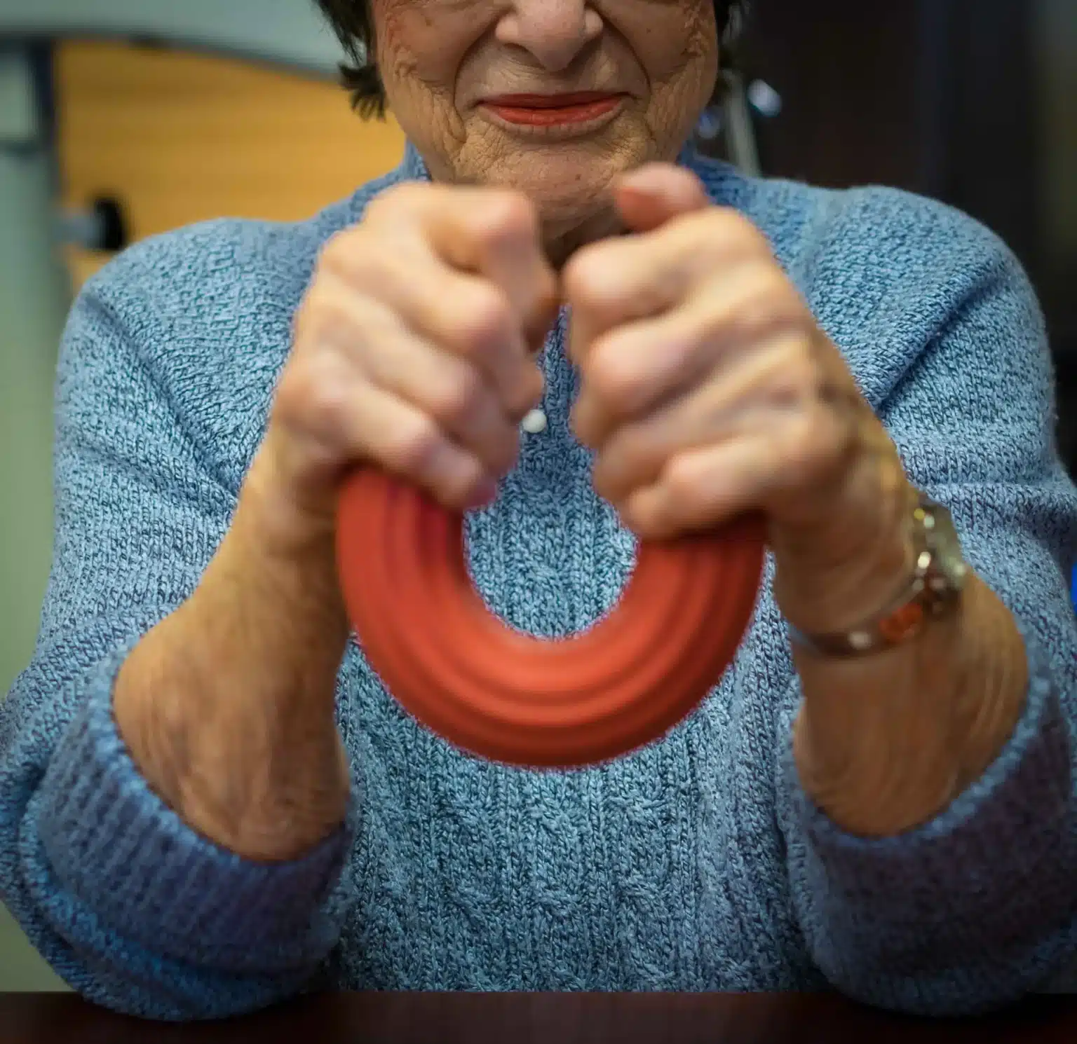 Close-up of a patient’s hands squeezing a red therapeutic ring to improve grip strength and manual dexterity.